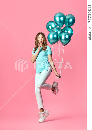 Full length portrait of happy surprised woman with blue balloons in hands on pink background. 77730811