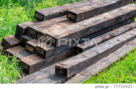 New railway sleepers impregnated with cryosote lie on green grass stacked on top of each other. 77733425