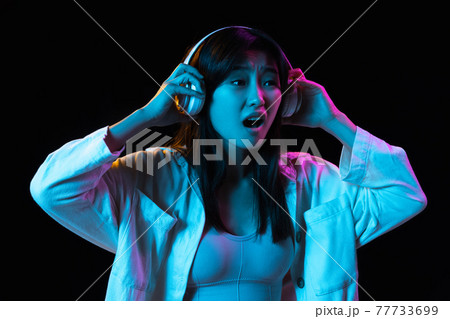 Asian young woman's portrait on dark studio background in neon. Concept of human emotions, facial expression, youth, sales, ad. 77733699