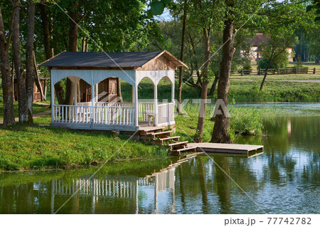 Summer gazebo on shore of pond. Wooden pergola in Merechevshchina village, Tadeusz Kosciuszko birthplace, Brest region, Belarus. 77742782