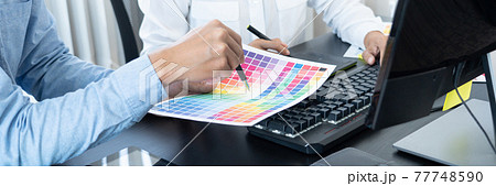 Graphic designer or creative working together coloring using graphics tablet and a stylus at desk with colleague. 77748590