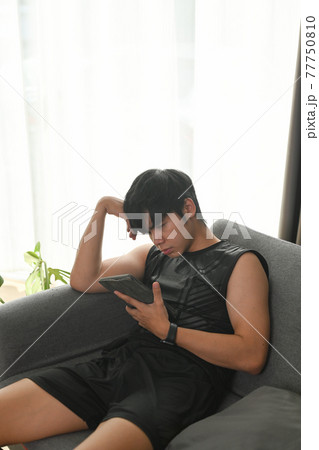 Young man using digital tablet and resting on sofa after exercising at home. Young man using digital tablet and resting on sofa after exercising at home. 77750810