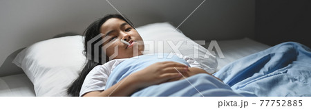 A little sick girl in a blanket is lying on the bed and measuring the temperature by her self. A little sick girl in a blanket is lying on the bed and measuring the temperature by her self. 77752885