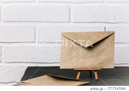 Blank envelope made of craft paper stands on a stand on a black table, communication concept in retro style, postal background with copy space 77754594
