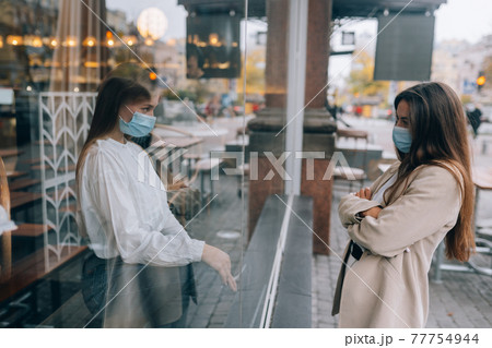 Two women in protective masks opposite each other, window between them. 77754944