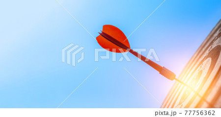 Red dart arrows in the center target of dartboard over sky background, target center business goal concept. Red dart arrows in the center target of dartboard over sky background, target center business goal concept. 77756362