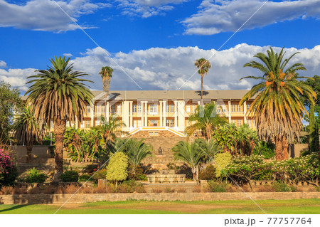 Park and garden with yellow palace building hidden behind tall palms, Windhoek, Namibia 77757764