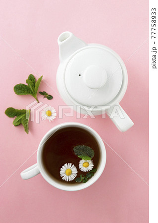 Cup and teapot of herbal tea with chamomile flowers and mint leaves on pink background Cup and teapot of herbal tea with chamomile flowers and mint leaves on pink background 77758933