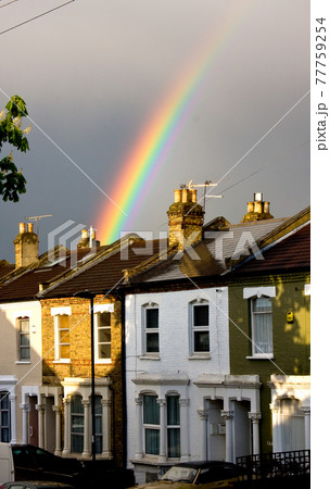 Rainbow emerges with sunlight behind terraced houses after rain Rainbow emerges with sunlight behind terraced houses after rain 77759254