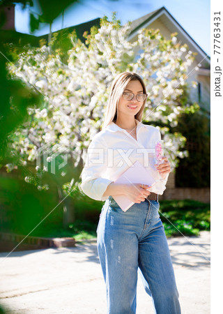 A woman in a white shirt and jeans with glasses in her hands in a spring garden. 77763431