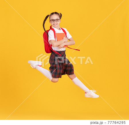 Excited schoolgirl jumping high in studio 77764295