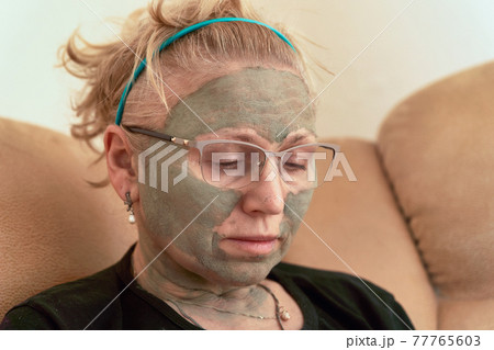 Grandmother with a cosmetic mask on her face made of healing clay Grandmother with a cosmetic mask on her face made of healing clay 77765603