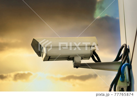 This is a security camera hanging on the wall of a building against the backdrop of a dramatic This is a security camera hanging on the wall of a building against the backdrop of a dramatic 77765874