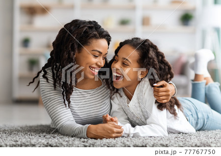 Happy african american mother and daughter laying on carpet 77767750