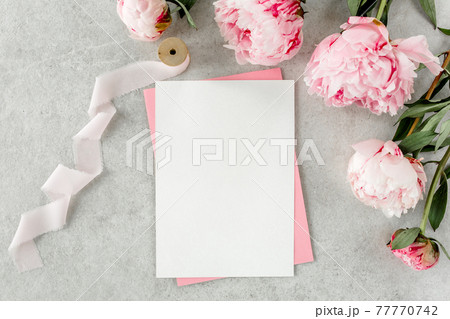 Mockup invitation, blank paper greeting card, pink envelope and peonies on gray stone table. Flower background. Flat lay, top view. Mockup invitation, blank paper greeting card, pink envelope and peonies on gray stone table. Flower background. Flat lay, top view. 77770742