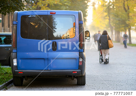Passenger van car parked on a city alley street side with blurred walking pedestrians in autumn. 77771007