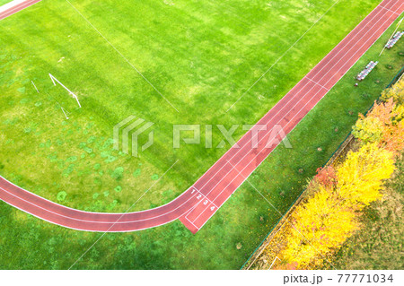 Aerial view of sports stadium with red running tracks and green grass football field. Aerial view of sports stadium with red running tracks and green grass football field. 77771034