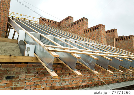 Unfinished brick apartment building with wooden roof structure under construction. Unfinished brick apartment building with wooden roof structure under construction. 77771266