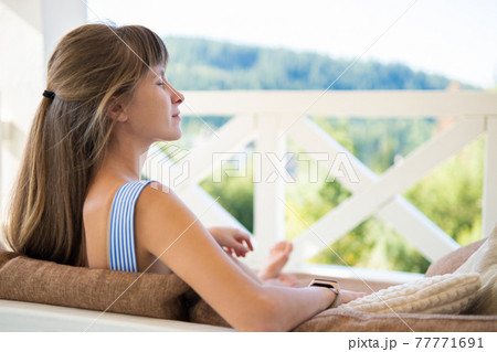 Young happy brunette woman lying down on terrace sofa with soft pillows enjoying warm summer day. Concept of free time on fresh air. Young happy brunette woman lying down on terrace sofa with soft pillows enjoying warm summer day. Concept of free time on fresh air. 77771691