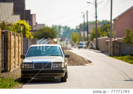 Front view of silver car parked on paved street in quiet area on sunny day at stone fence of residential cottage. Transportation and urban parking concept. 77771765