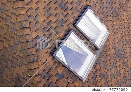 Close-up of new small attic plastic windows installed in brown shingled house roof. Professionally done building and construction work, roofing and installation concept. Close-up of new small attic plastic windows installed in brown shingled house roof. Professionally done building and construction work, roofing and installation concept. 77772099