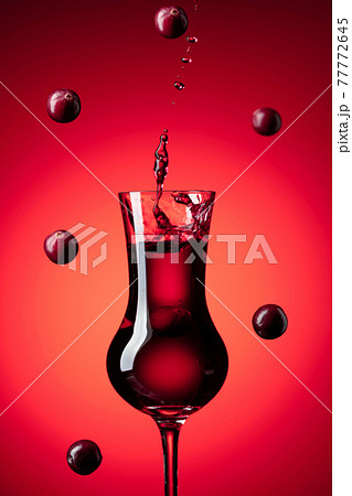 Cranberry liquor with falling berries on a red background. 77772645