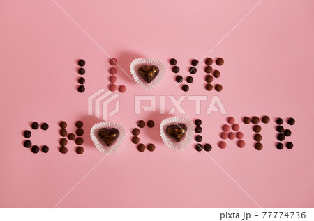 Flat lay of I LOVE CHOCOLATE lettering laid out from multi colored chocolate pills and pralines on pink background with copy space 77774736