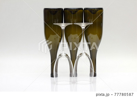 Three empty upturned wine bottles and two glasses on a white background. 77780587