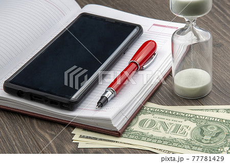 Hourglass, money, pen and notebook are on the table. Business office items.  77781429