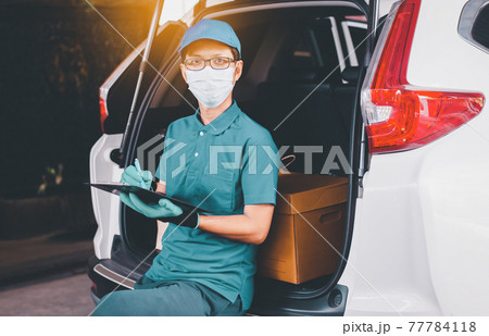 Delivery man employee checking list on clipboard standing in front of van during coronavirus pandemic situation Delivery man employee checking list on clipboard standing in front of van during coronavirus pandemic situation 77784118