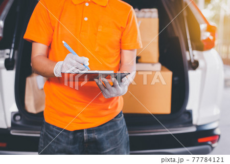 Delivery man employee checking list on clipboard standing in front of van during coronavirus pandemic situation 77784121