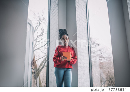 Positive african american woman with a laptop standing near the window 77788654
