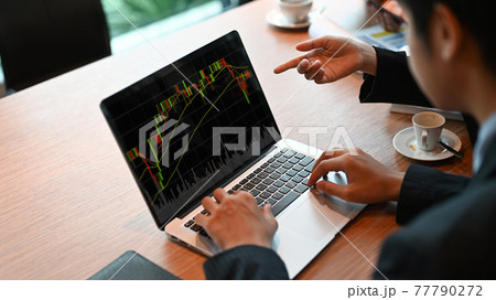 Business People are using a computer laptop with a candlestick chart on-screen at the meeting table. 77790272