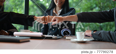 Businesspeople are greeting each other with hand bumping while sitting at the meeting table. 77790278