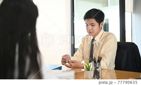 A businessman is sitting and talking with colleagues at the wooden working table. 77790635