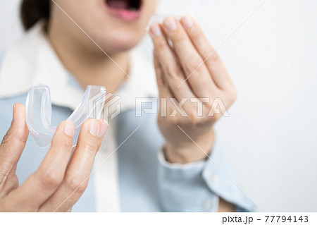 Hands of lady girl with occlusal splint to protect teeth from grinding caused by bruxism,woman patient holding bite plate silicone rubber guard night,medical equipment used to wear teeth while sleep 77794143