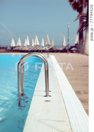 Hotel swimming pool side with blue water, close-up shot, with sunbeds on background 77794426