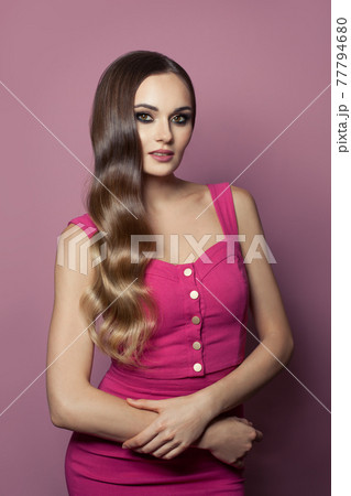 Glamorous model woman with long hair wearing pink dress posing on pink background Glamorous model woman with long hair wearing pink dress posing on pink background 77794680