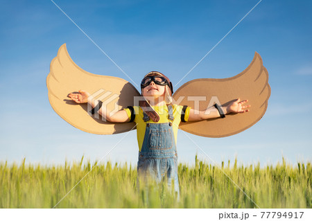 Happy child with cardboard wings playing outdoor in summer 77794917