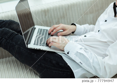 young man looking at laptop screen while lying on sofa young man looking at laptop screen while lying on sofa 77794947