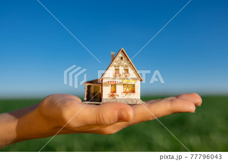 House in hand against spring green field and blue sky 77796043