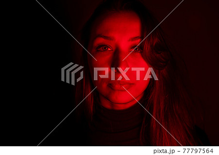 Young woman looks at camera in contrast red light, addiction, imprisonment 77797564
