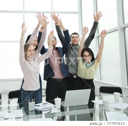 happy business team standing near the desktop with hands up happy business team standing near the desktop with hands up 77797613