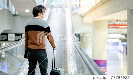 Male tourist carrying suitcase luggage on travelator 77797927