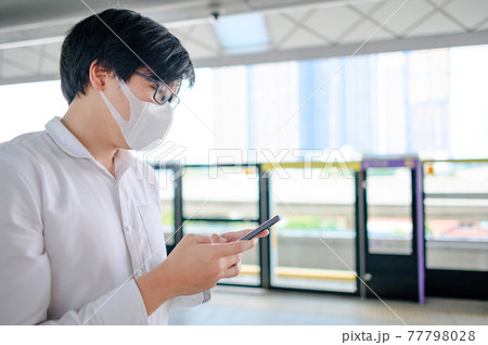 Man wearing mask using phone at skytrain station Man wearing mask using phone at skytrain station 77798028