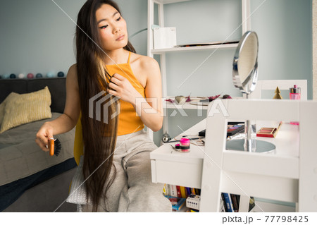 Woman looking at her reflection in mirror and brushing her long hair 77798425