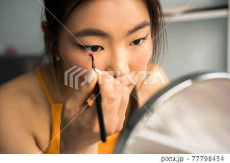 Woman looking at the hand mirror and preparing makeup at home at the weekend 77798434