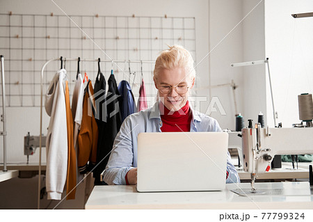 Designer working at his laptop with pleasure smile while creating new collection Designer working at his laptop with pleasure smile while creating new collection 77799324