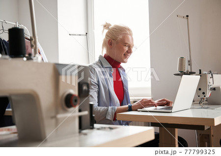 Man looking at the laptop screen while working at the table near sewing machine 77799325
