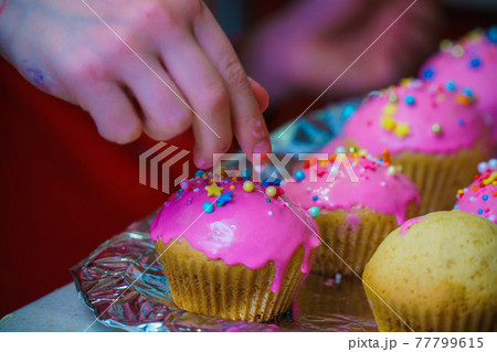 Freshly baked vanilla muffins are garnished with sweet icing and topping. 77799615